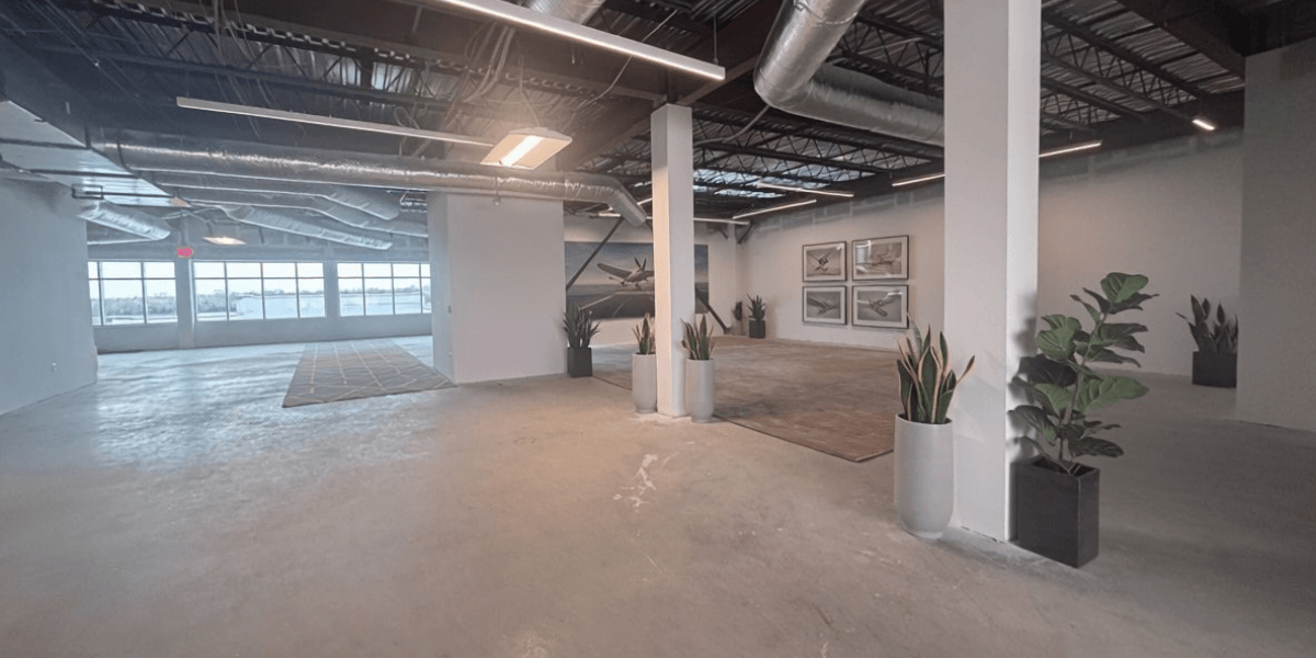 Open third-floor office space at Chantilly Air with polished concrete, exposed steel ceiling, runway-view windows, and aviation art.