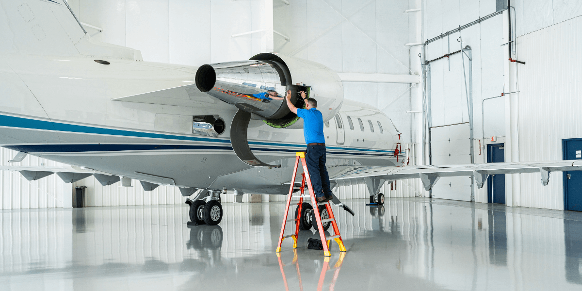 A Chantilly Air maintenance technician on a ladder doing maintenance on a private charter airplane inside of Chantilly Air Jet Center hangar.