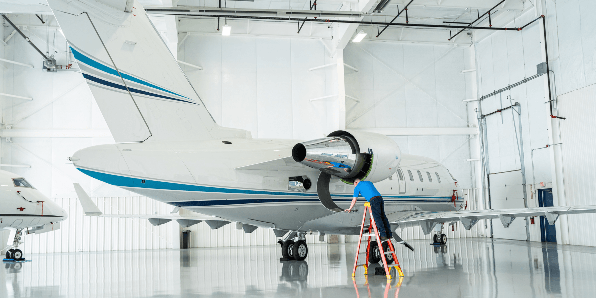 Certified A&P technician performing business jet maintenance on an exposed turbofan engine inside a Part 145 repair station hangar