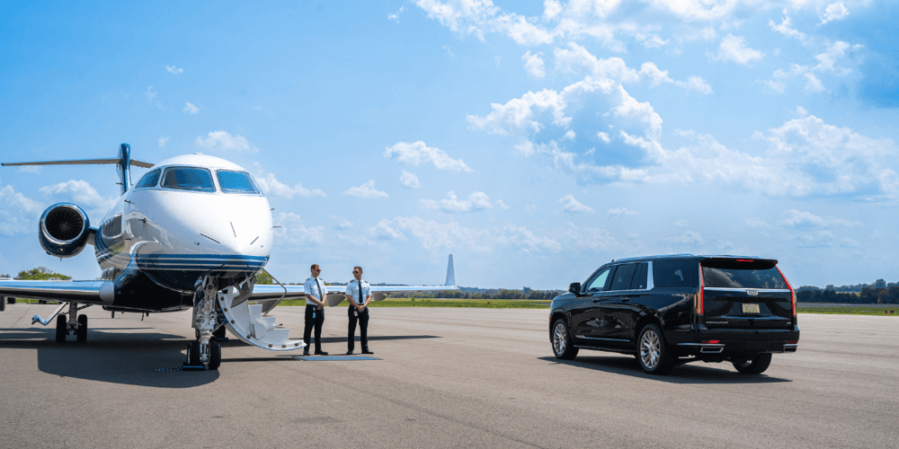 Two pilots waiting beside an aircraft with a black SUV parked near by.