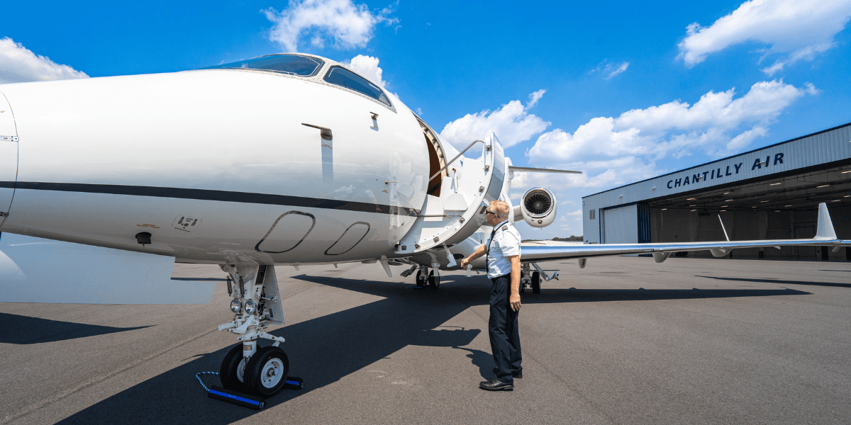 Chantilly Air pilot performing a preflight inspection of a private jet on the ramp at Washington Manassas Airport, with the Chantilly Air hangar in the background