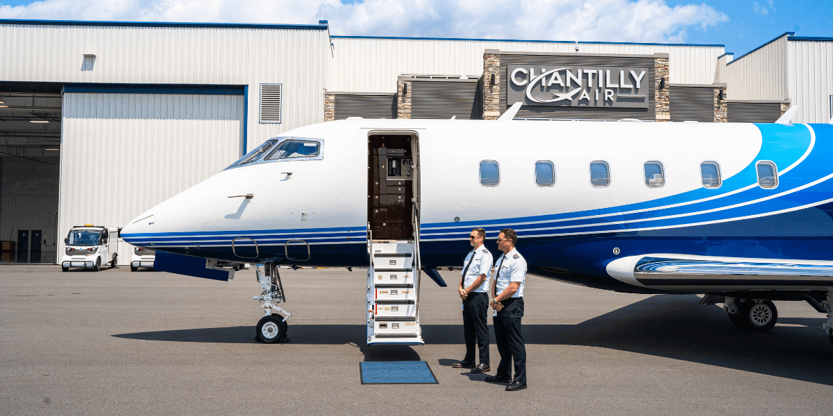 Two pilots standing outside of a private aircraft with the steps open to the plane, awaiting guests