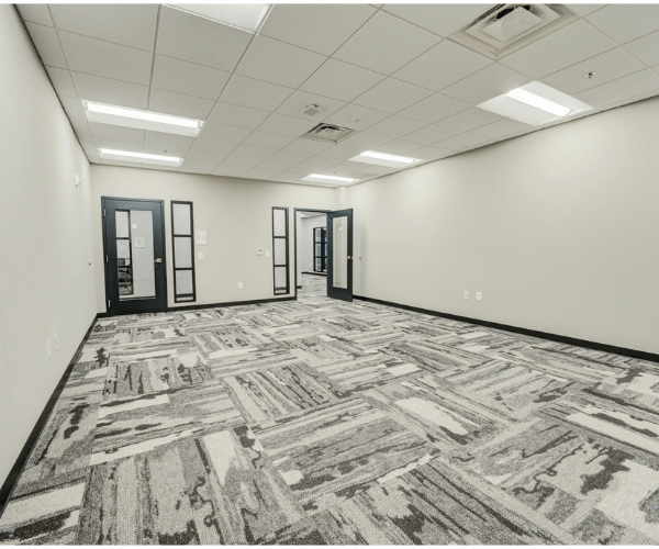 Empty modern office suite with patterned carpet, glass interior doors, and drop ceiling lighting in a professional aviation business center.