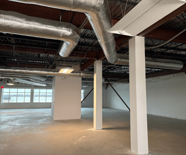 Open commercial office space with exposed ceilings, HVAC ductwork, concrete floors, and structural columns ready for build-out in an aviation facility.