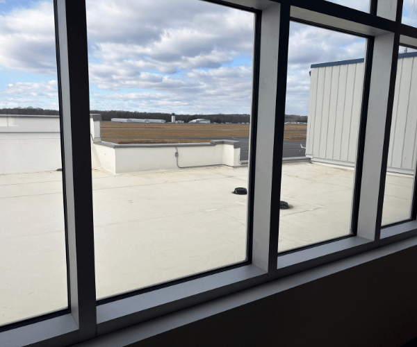 Office window view overlooking airport rooftops and airfield operations, providing direct visibility of aviation activity from a jet center workspace.