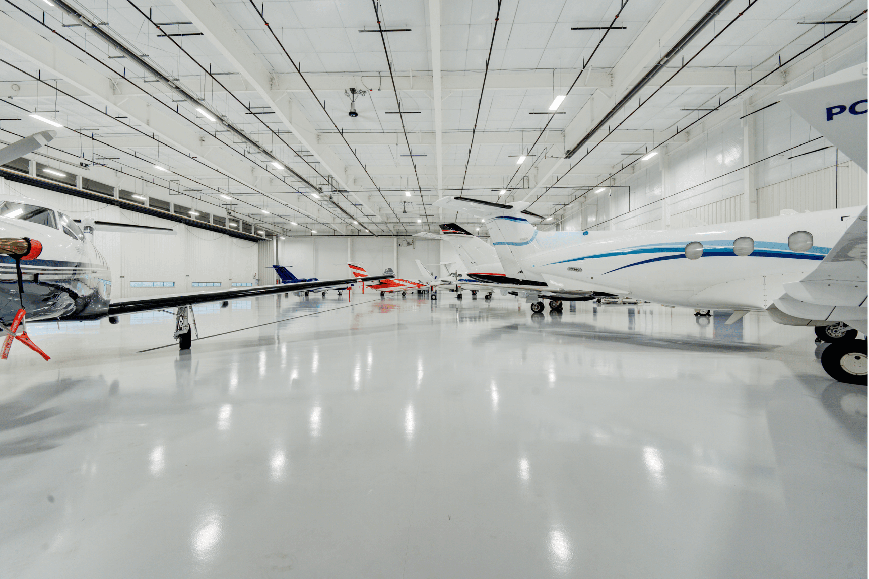 A wide shot of several aircrafts stored in the all white Chantilly Air hangar.