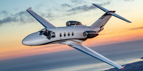 Light jet flying in the sky over a body of water at sunset