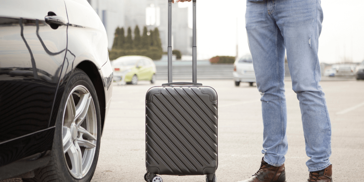 Suitcase and person standing next to rental car.