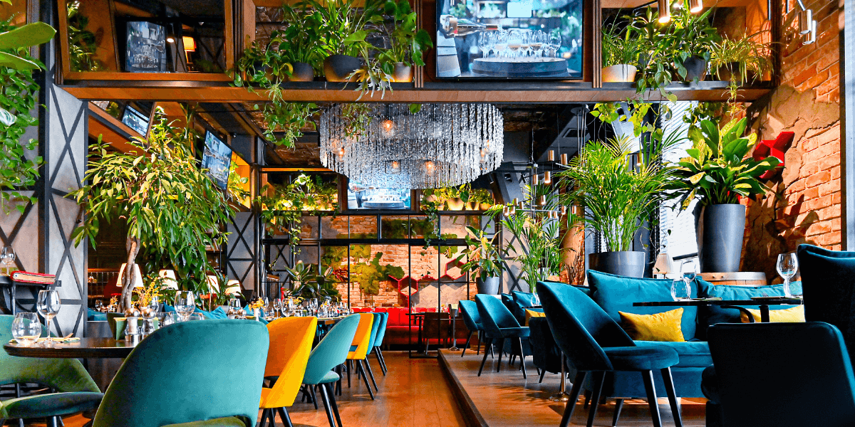 A colorful restaurant with large chandeliers and ferns hanging from the ceiling.