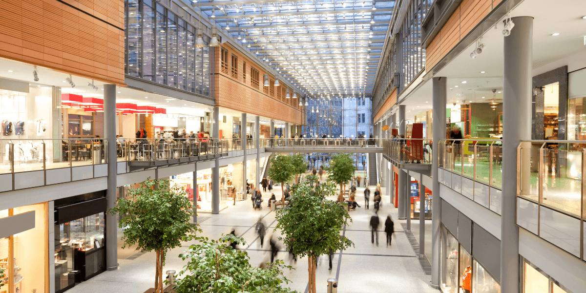 A white, wood and silver two story shopping mall with small trees in the center.